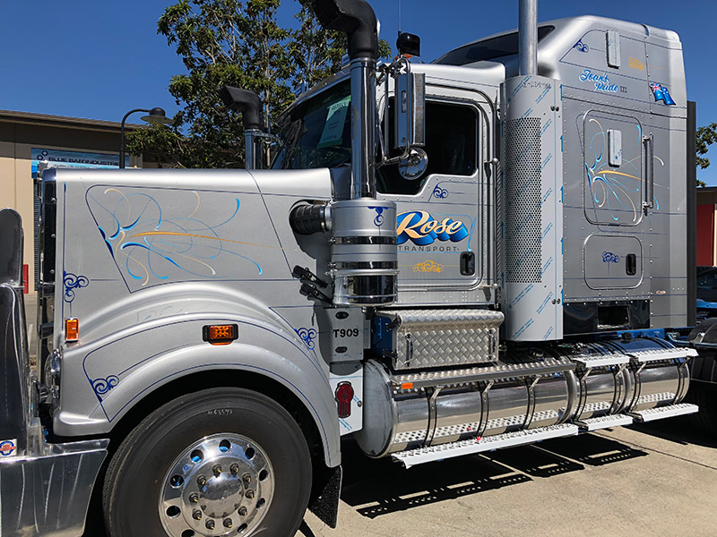 Silver Kenworth prime mover with Rose Transport lettering and flowing blue and gold pinstripe scrolls